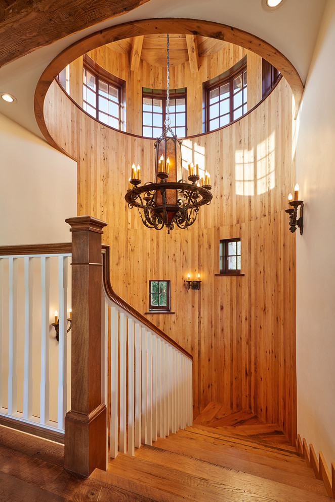 На фото: большая изогнутая деревянная лестница в стиле рустика с деревянными ступенями с