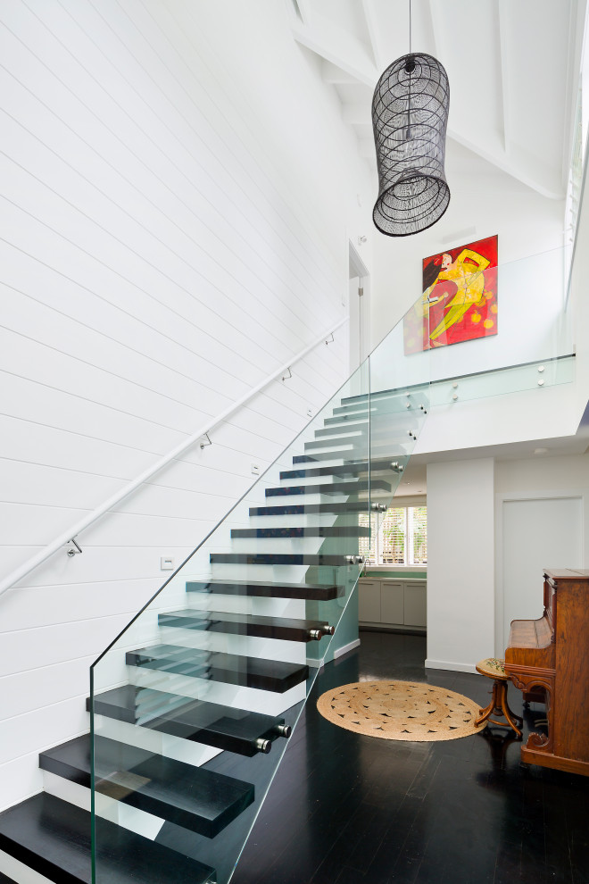 Пример оригинального дизайна: большая прямая лестница в морском стиле с деревянными ступенями, стеклянными перилами и панелями на стенах без подступенок