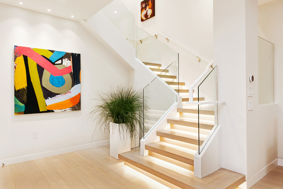 Cette image montre un escalier design en U avec des marches en bois, des contremarches en bois, un garde-corps en verre et éclairage.