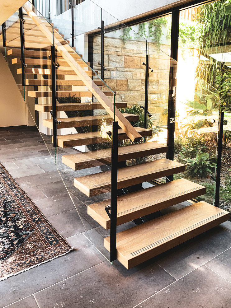 Modelo de escalera recta contemporánea grande con escalones de madera, contrahuellas de vidrio y barandilla de varios materiales