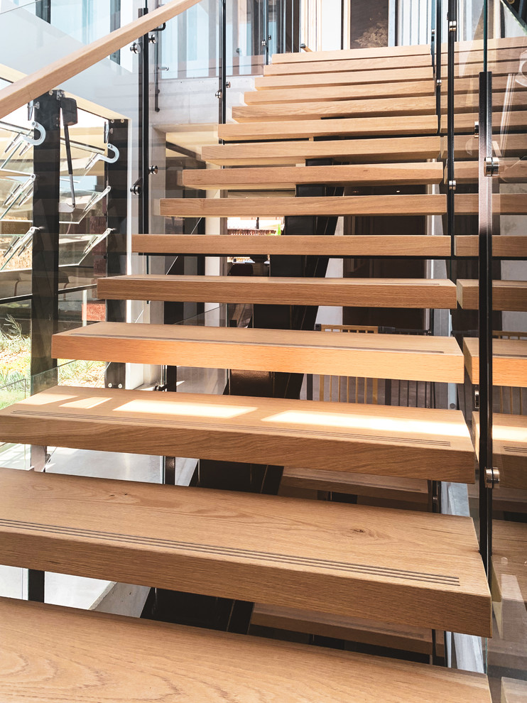 Diseño de escalera recta actual grande con escalones de madera, contrahuellas de vidrio y barandilla de varios materiales