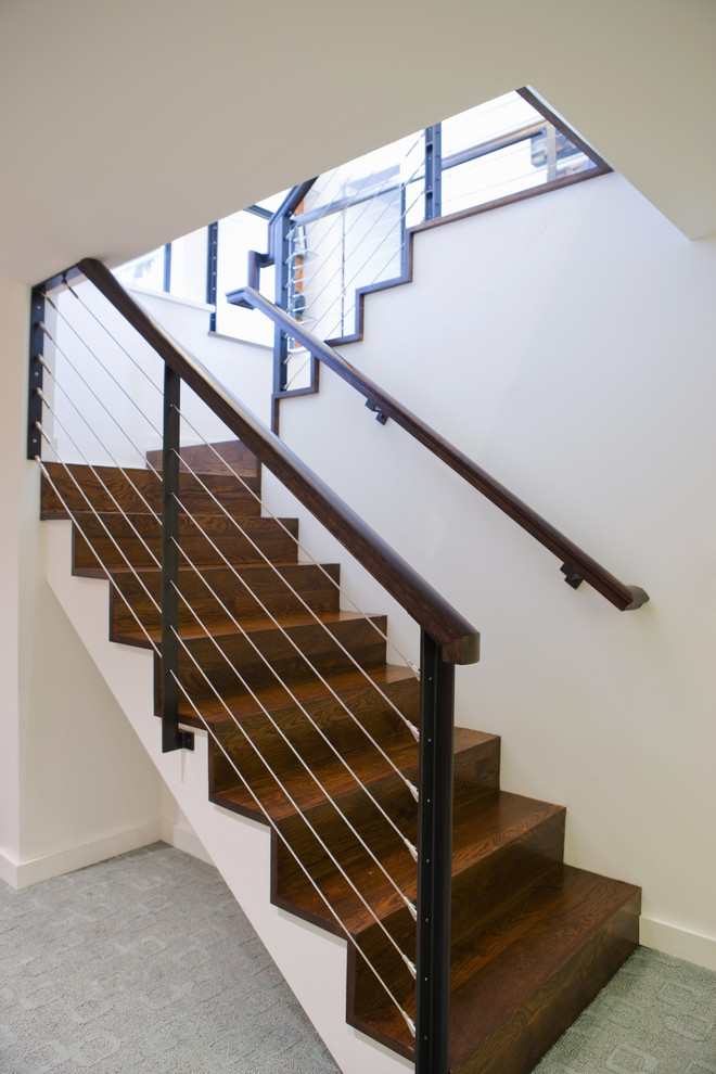 Diseño de escalera minimalista con escalones de madera, contrahuellas de madera y barandilla de cable