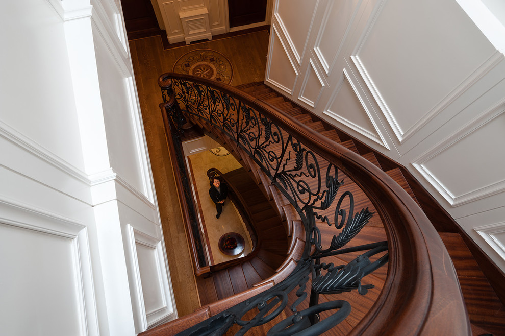This is an example of a large classic wood curved staircase in New York with wood risers.