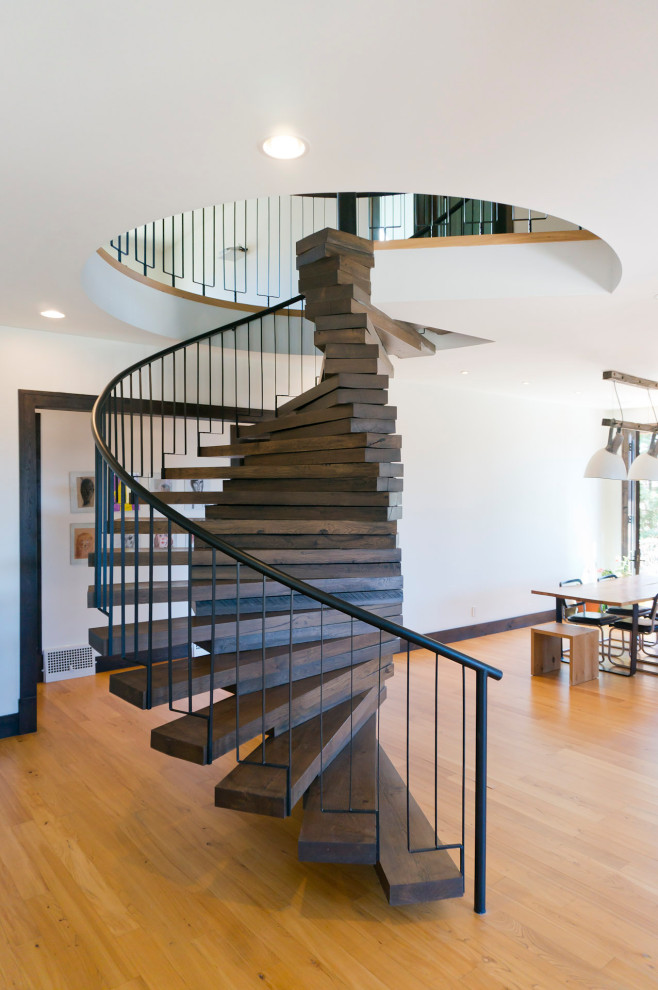 Immagine di una grande scala a chiocciola minimalista con pedata in legno, alzata in legno e parapetto in metallo