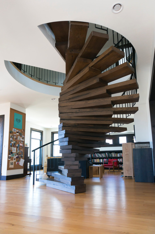 Immagine di una grande scala a chiocciola moderna con pedata in legno, alzata in legno e parapetto in metallo