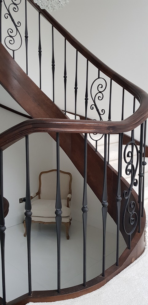 Imagen de escalera curva tradicional grande con escalones de madera, contrahuellas de madera y barandilla de metal