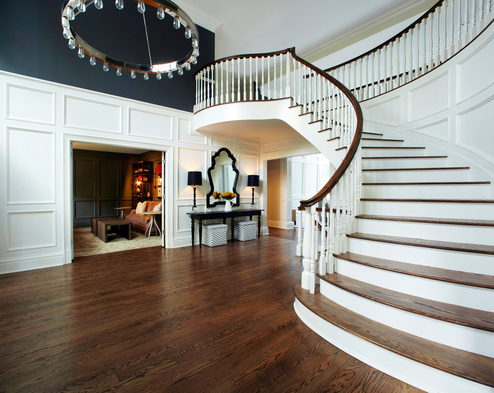 На фото: огромная изогнутая лестница в классическом стиле с деревянными ступенями и крашенными деревянными подступенками