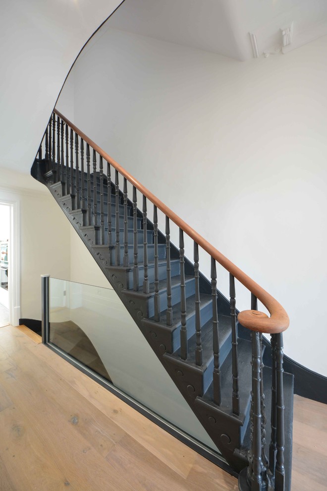 This is an example of an expansive contemporary painted wood curved staircase in Kent with painted wood risers.