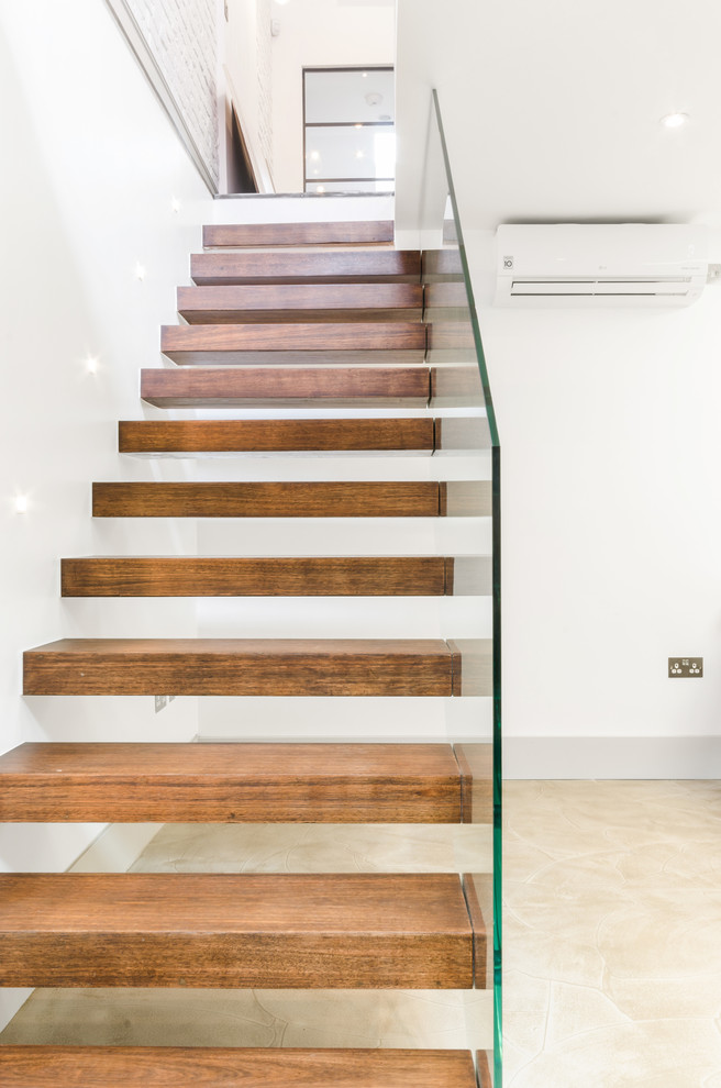 This is an example of a contemporary wood floating glass railing staircase in London with open risers.
