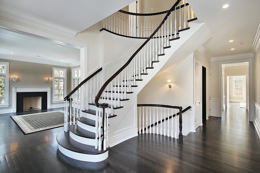 Стильный дизайн: большая изогнутая лестница в классическом стиле с деревянными ступенями, крашенными деревянными подступенками и деревянными перилами - последний тренд