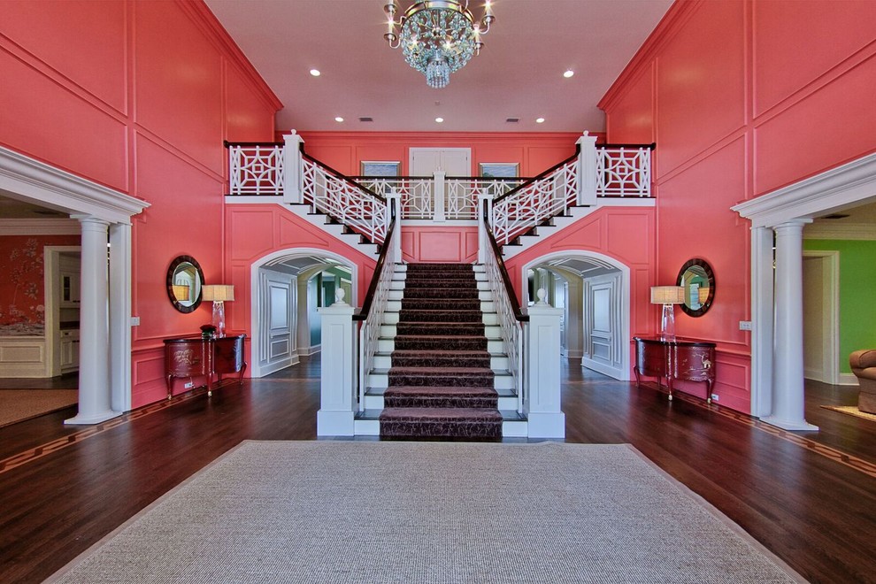 На фото: огромная угловая лестница в классическом стиле с ступенями с ковровым покрытием, ковровыми подступенками и деревянными перилами с
