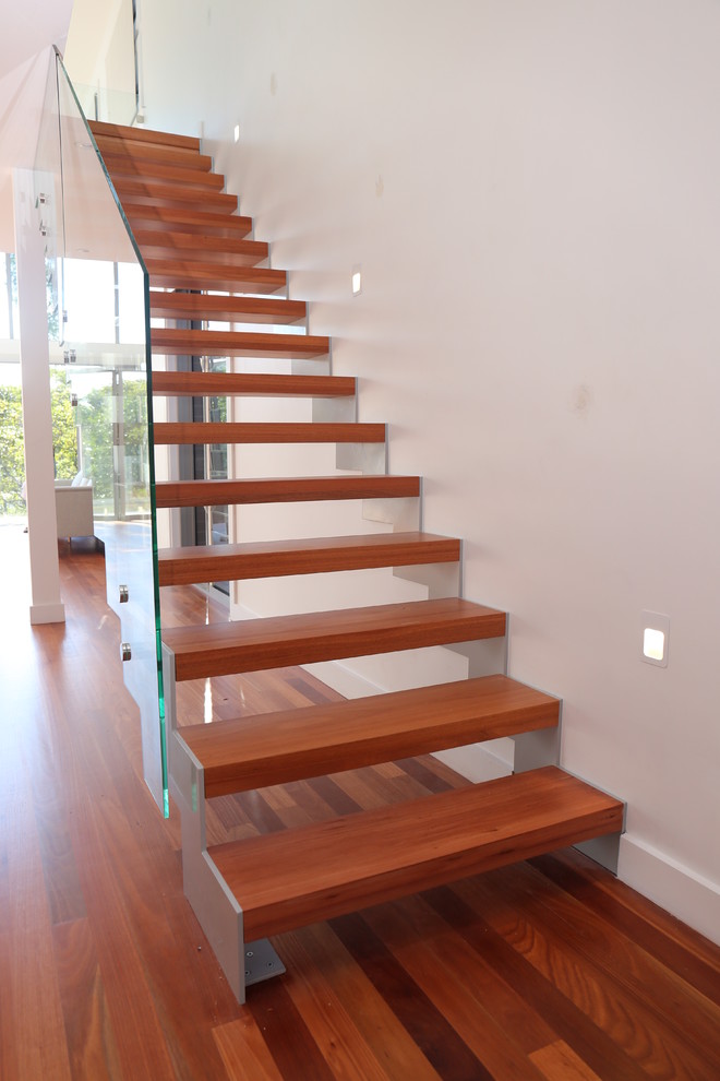 Immagine di una scala a rampa dritta minimalista di medie dimensioni con pedata in legno, nessuna alzata e parapetto in vetro