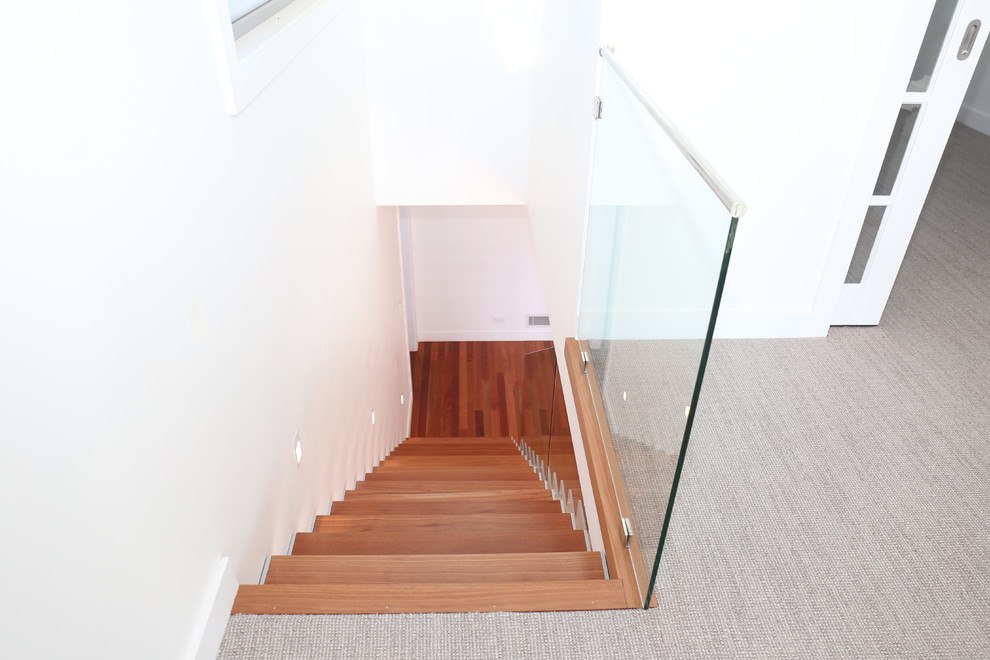 Ejemplo de escalera recta moderna de tamaño medio sin contrahuella con escalones de madera y barandilla de vidrio