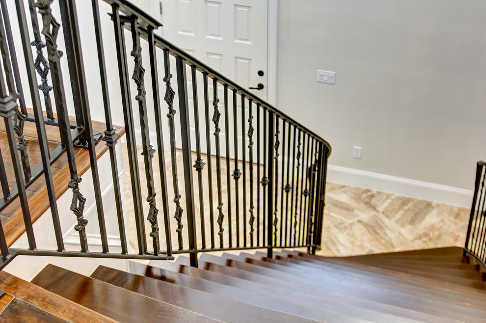Diseño de escalera curva clásica grande con escalones de madera, contrahuellas con baldosas y/o azulejos y barandilla de metal