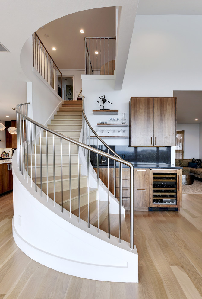 Idée de décoration pour un escalier courbe design avec des marches en bois, des contremarches en bois, un garde-corps en métal et rangements.