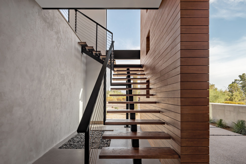 This is an example of a contemporary wood floating wire cable railing staircase in Phoenix with open risers and wood walls.