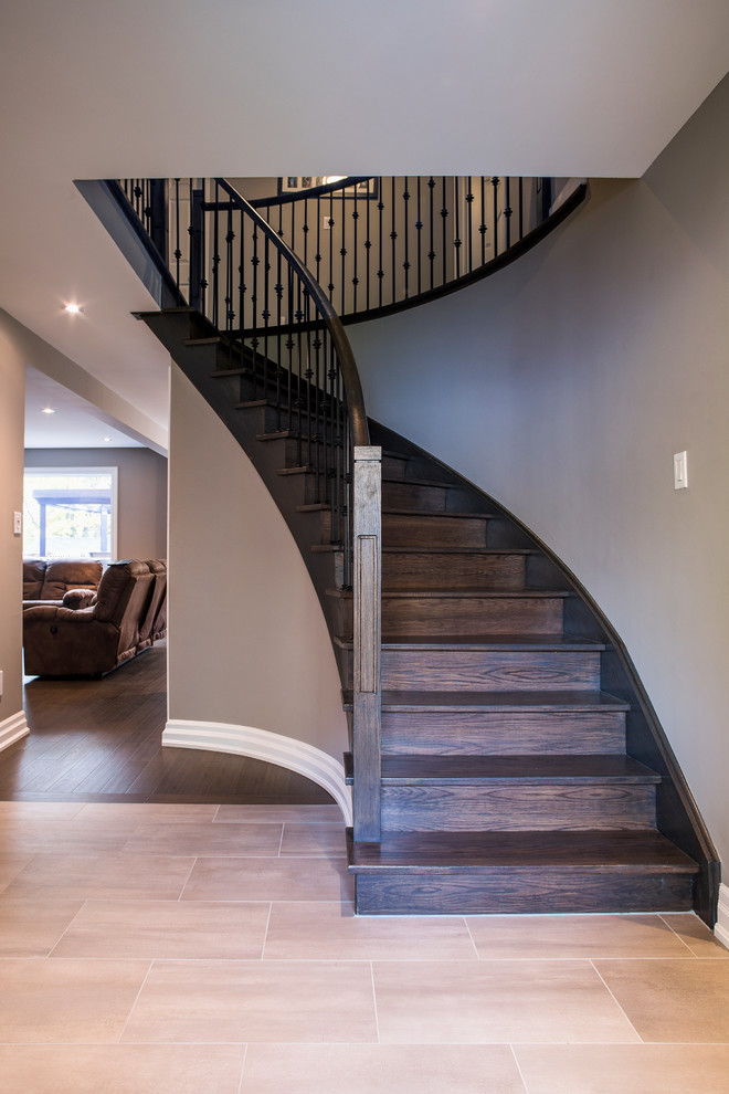 Photo of a large traditional wood spiral metal railing staircase in Toronto with wood risers.