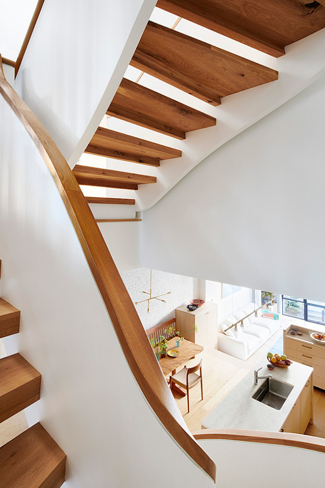 Пример оригинального дизайна: огромная изогнутая лестница в стиле ретро с деревянными ступенями и перилами из смешанных материалов без подступенок