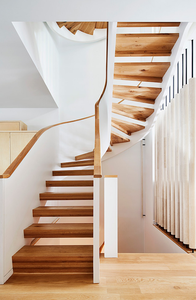 Идея дизайна: огромная изогнутая лестница в стиле ретро с деревянными ступенями и перилами из смешанных материалов без подступенок