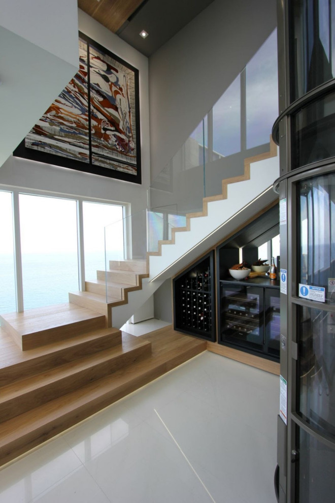 Стильный дизайн: большая угловая деревянная лестница в стиле модернизм с деревянными ступенями, стеклянными перилами и обоями на стенах - последний тренд