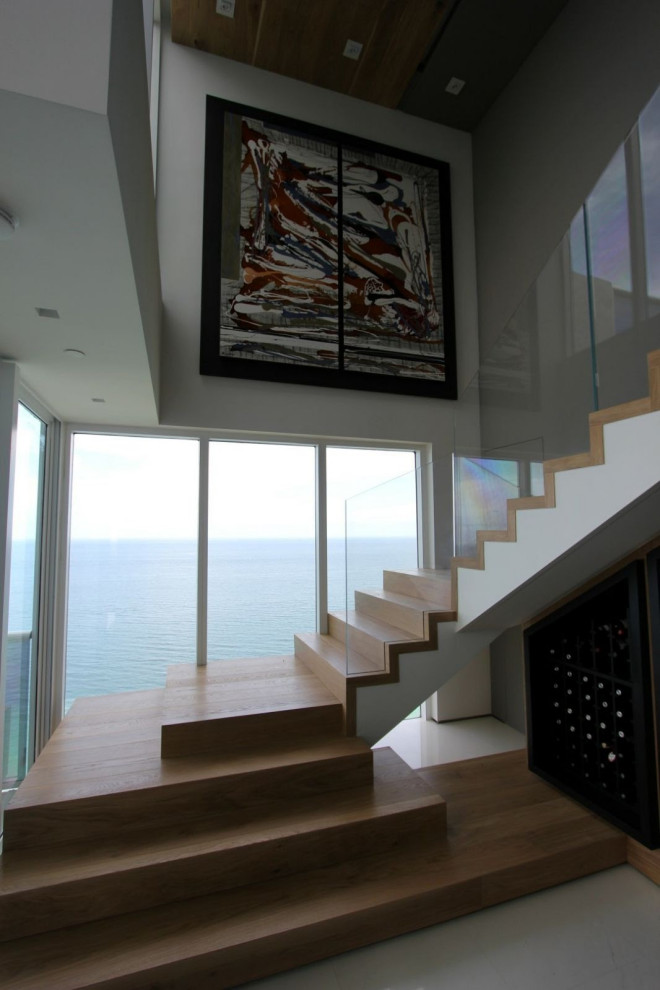 Modelo de escalera en L minimalista grande con escalones de madera, contrahuellas de madera, barandilla de vidrio y papel pintado