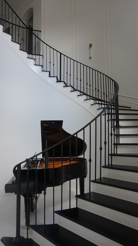 Modelo de escalera curva actual grande con escalones de madera, contrahuellas de madera pintada y barandilla de metal