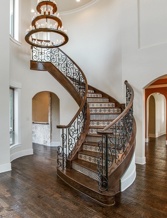 Aménagement d'un escalier courbe méditerranéen avec des marches en bois, des contremarches carrelées et un garde-corps en métal.