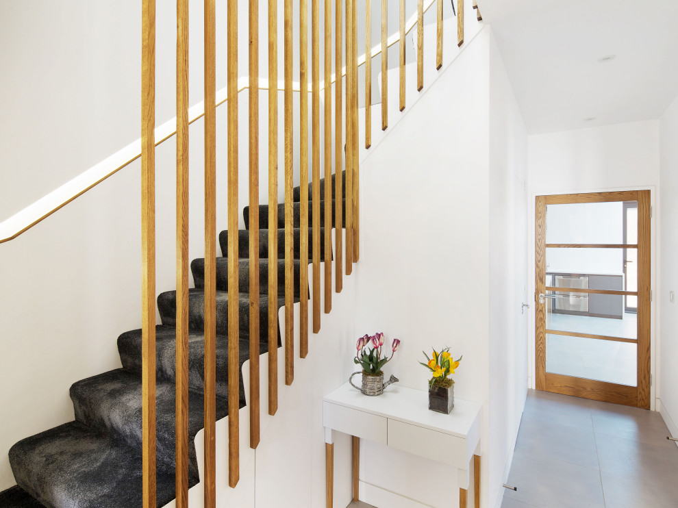 Photo of a medium sized modern carpeted l-shaped wood railing staircase in London with carpeted risers.