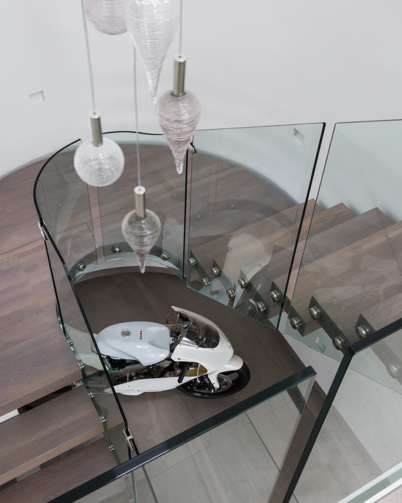 Cette image montre un grand escalier sans contremarche courbe design avec des marches en bois et un garde-corps en verre.