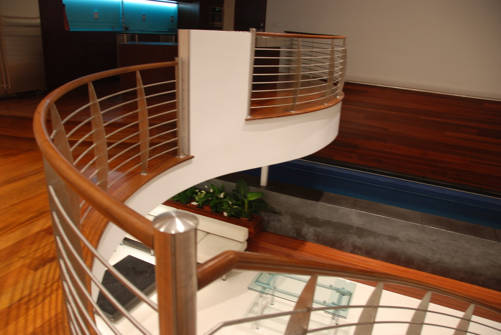 Diseño de escalera curva minimalista grande con escalones de madera, contrahuellas de metal y barandilla de cable