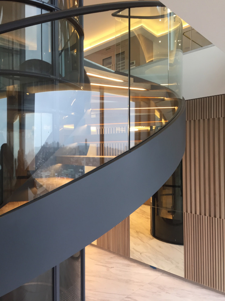 Свежая идея для дизайна: большая изогнутая лестница в современном стиле с деревянными ступенями и стеклянными перилами без подступенок - отличное фото интерьера
