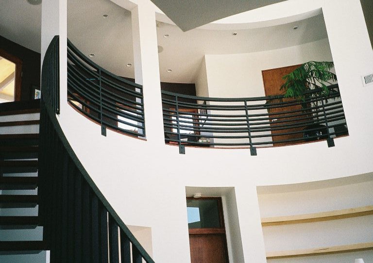 Réalisation d'un escalier sans contremarche courbe minimaliste avec des marches en bois et un garde-corps en métal.