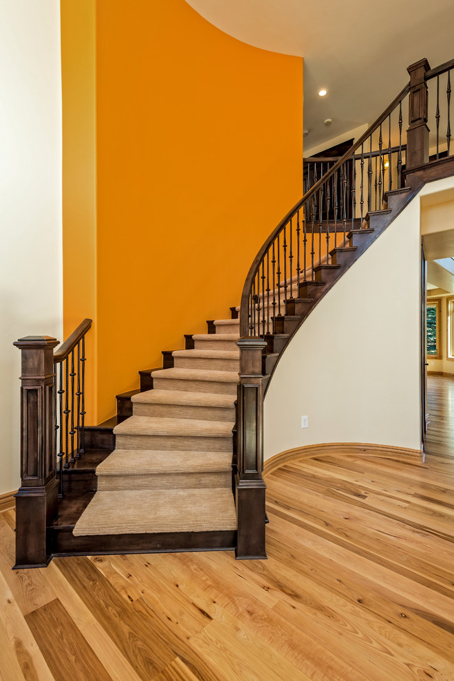 Пример оригинального дизайна: большая изогнутая деревянная лестница в стиле неоклассика (современная классика) с ступенями с ковровым покрытием