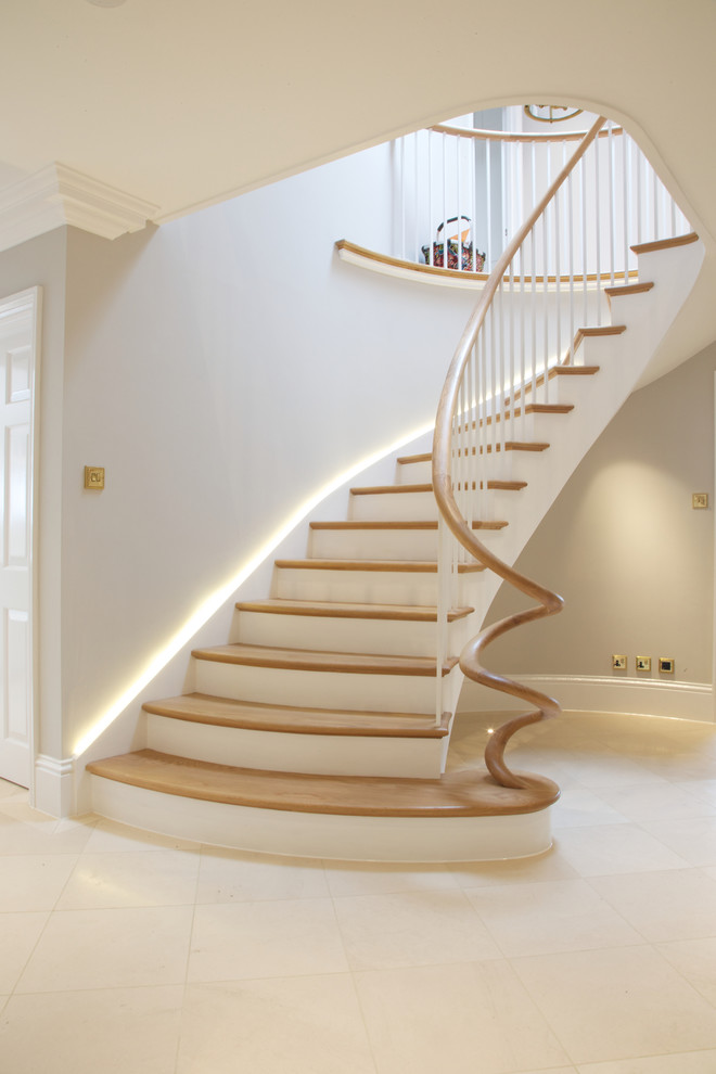 Свежая идея для дизайна: изогнутая лестница в стиле неоклассика (современная классика) с деревянными ступенями и крашенными деревянными подступенками - отличное фото интерьера