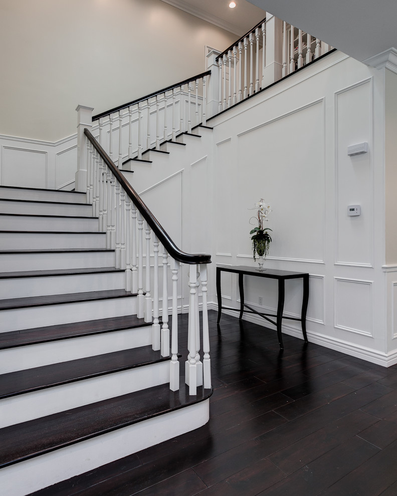 Пример оригинального дизайна: большая угловая лестница в классическом стиле с деревянными ступенями и крашенными деревянными подступенками