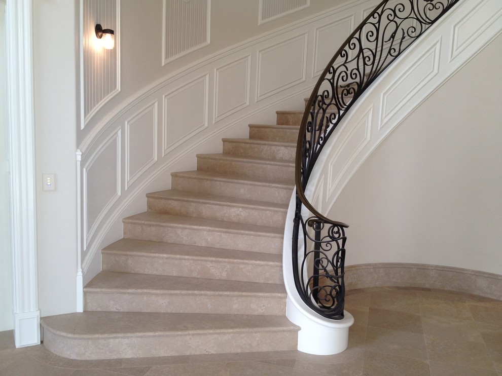 На фото: изогнутая лестница в стиле ретро с ступенями с ковровым покрытием, ковровыми подступенками, металлическими перилами и панелями на стенах