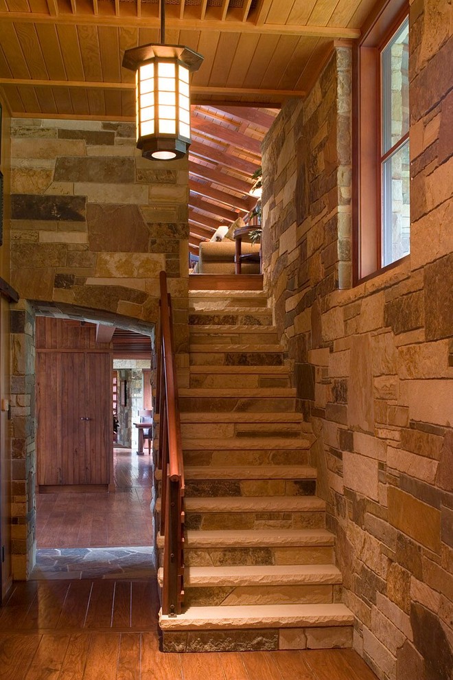 オースティンにある高級な中くらいなラスティックスタイルのおしゃれな直階段 (トラバーチンの蹴込み板、木材の手すり) の写真