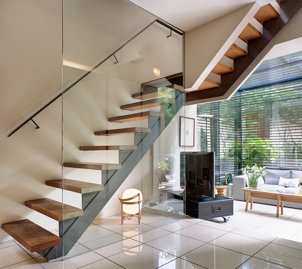 Aménagement d'un escalier courbe moderne de taille moyenne avec des marches en bois, des contremarches en verre et un garde-corps en métal.