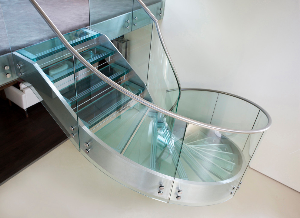 Photo of a large contemporary glass spiral metal railing staircase in Gloucestershire with glass risers.