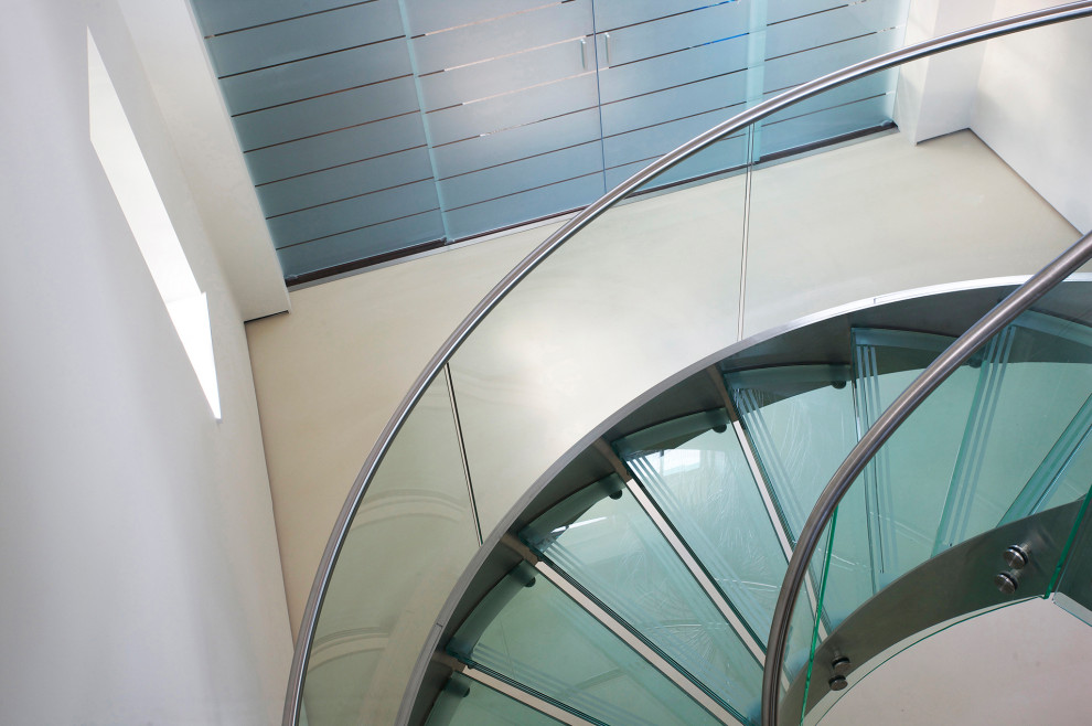 Пример оригинального дизайна: большая винтовая лестница в современном стиле с стеклянными ступенями, стеклянными подступенками и металлическими перилами