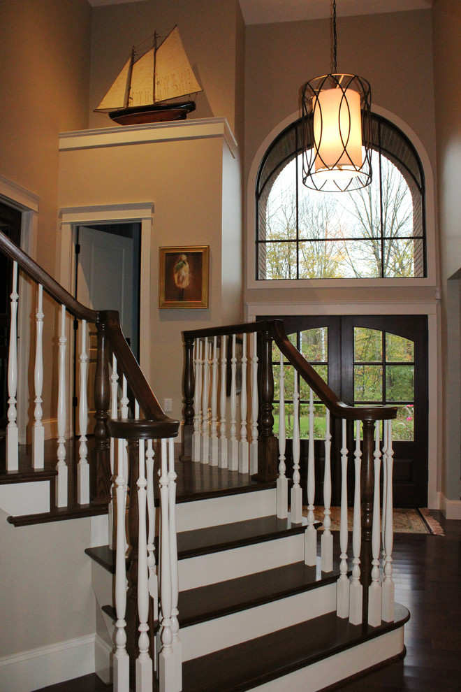 На фото: большая изогнутая деревянная лестница в классическом стиле с деревянными ступенями и деревянными перилами