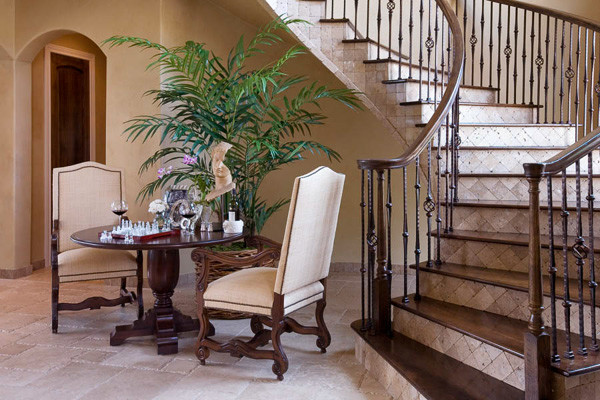 На фото: изогнутая лестница в средиземноморском стиле с деревянными ступенями, деревянными перилами и подступенками из травертина с