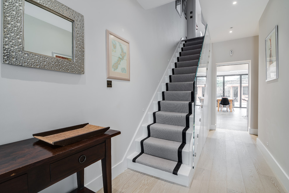 Imagen de escalera recta minimalista de tamaño medio con escalones enmoquetados, contrahuellas enmoquetadas y barandilla de vidrio
