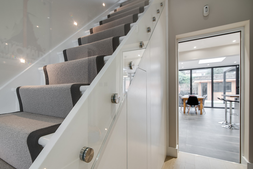 Inspiration for a medium sized modern carpeted straight glass railing staircase in London with carpeted risers.