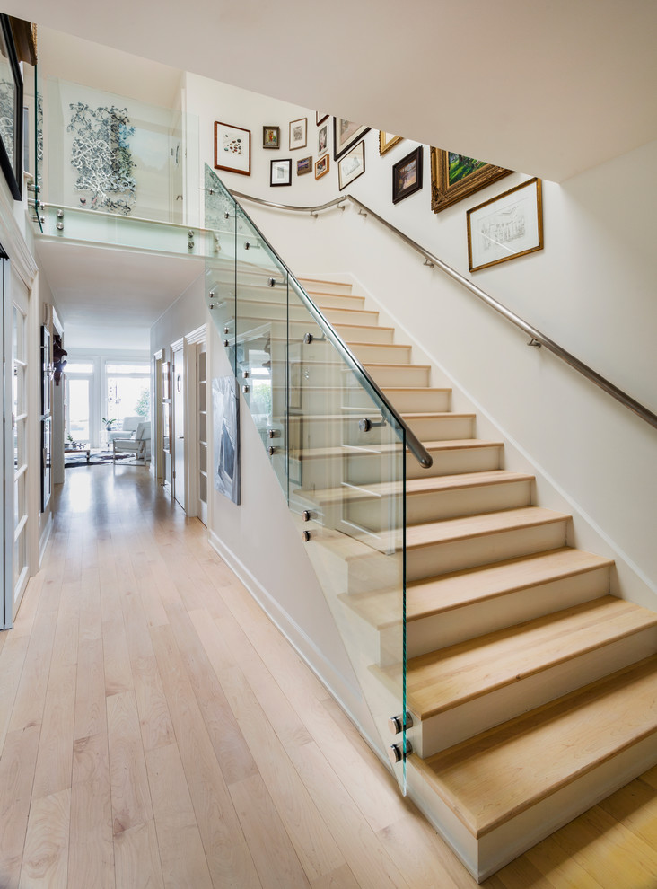 Cette image montre un grand escalier design en L avec des marches en bois, des contremarches en bois et un garde-corps en verre.