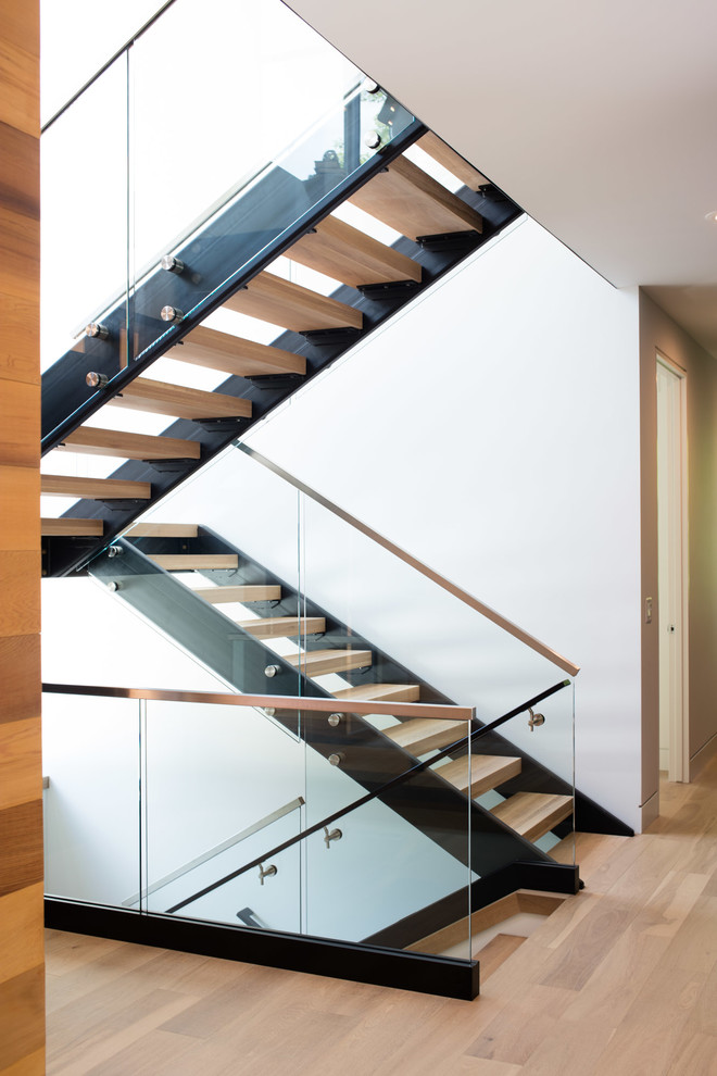 Пример оригинального дизайна: большая лестница на больцах в современном стиле с деревянными ступенями и стеклянными перилами без подступенок