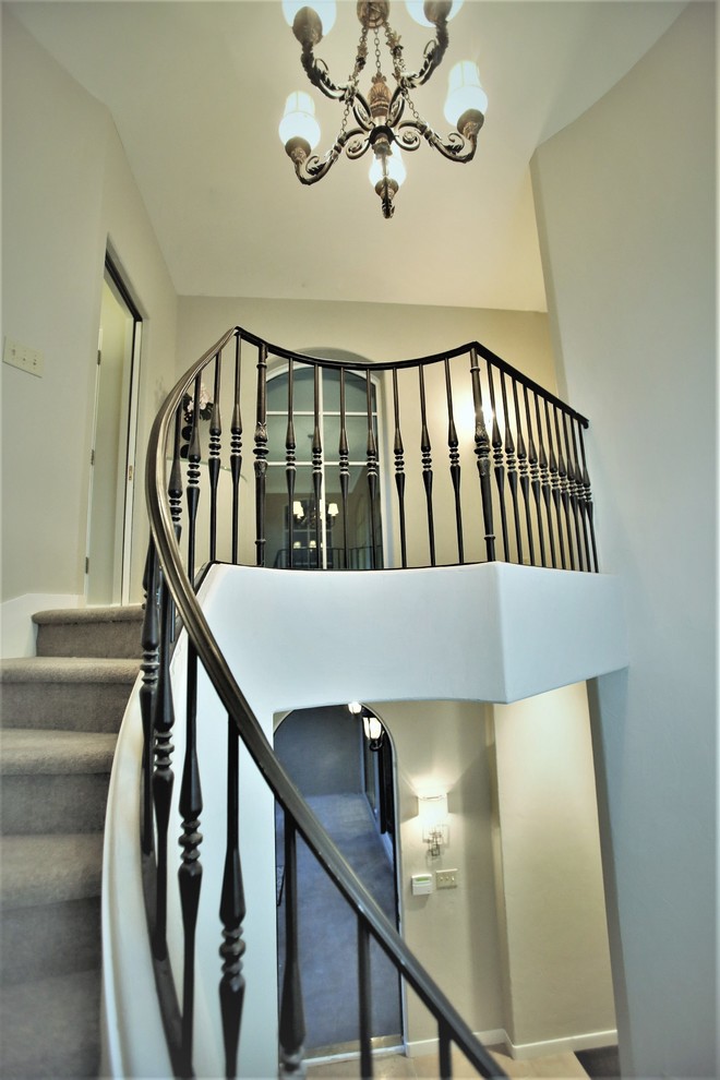 На фото: огромная изогнутая деревянная лестница в стиле неоклассика (современная классика) с ступенями с ковровым покрытием и металлическими перилами