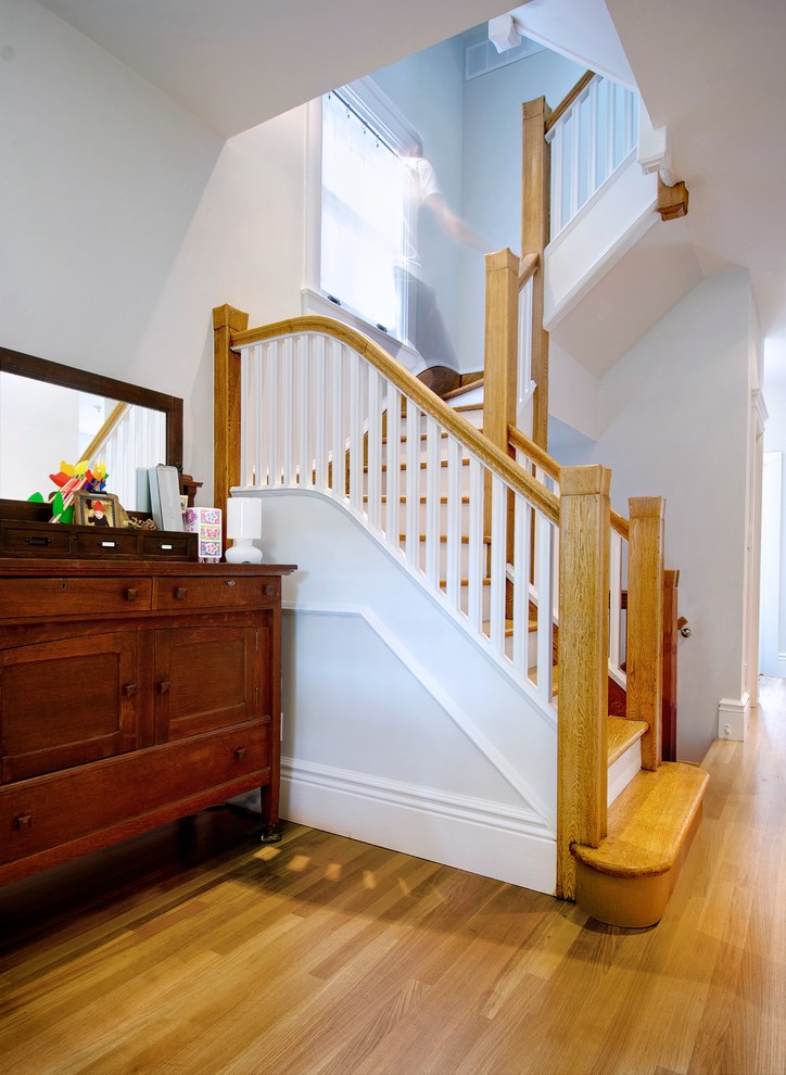 На фото: угловая деревянная лестница среднего размера в стиле неоклассика (современная классика) с деревянными ступенями и деревянными перилами с