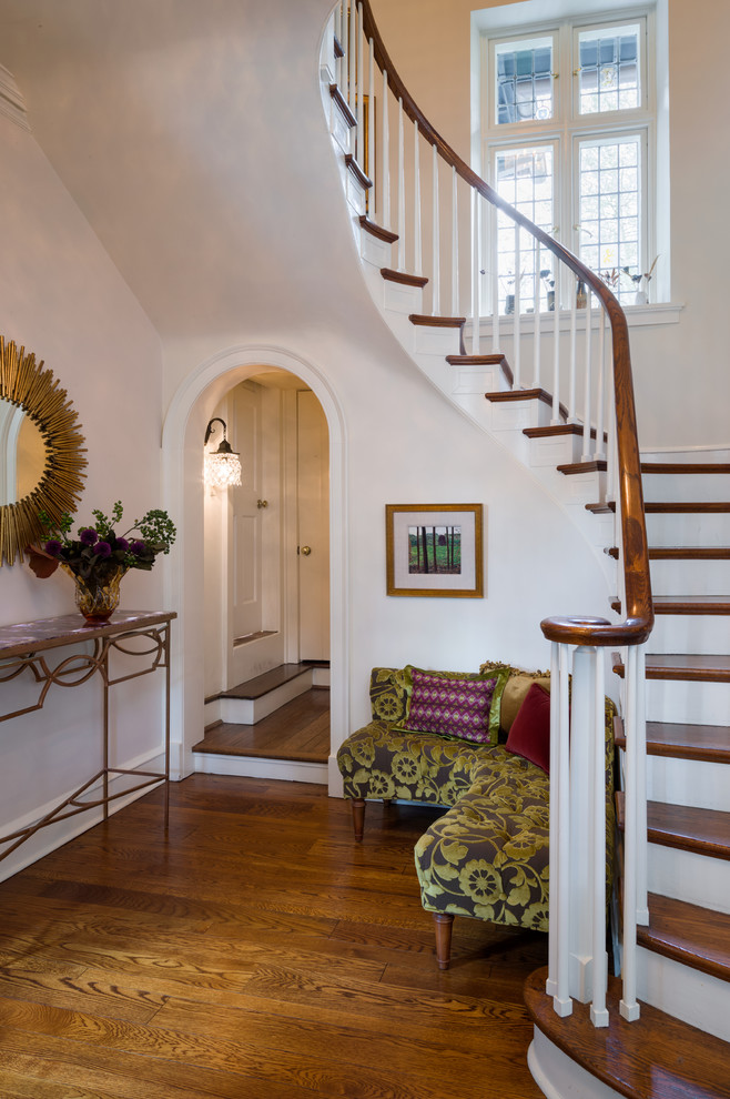 Imagen de escalera curva clásica grande con escalones de madera, contrahuellas de madera pintada y barandilla de madera