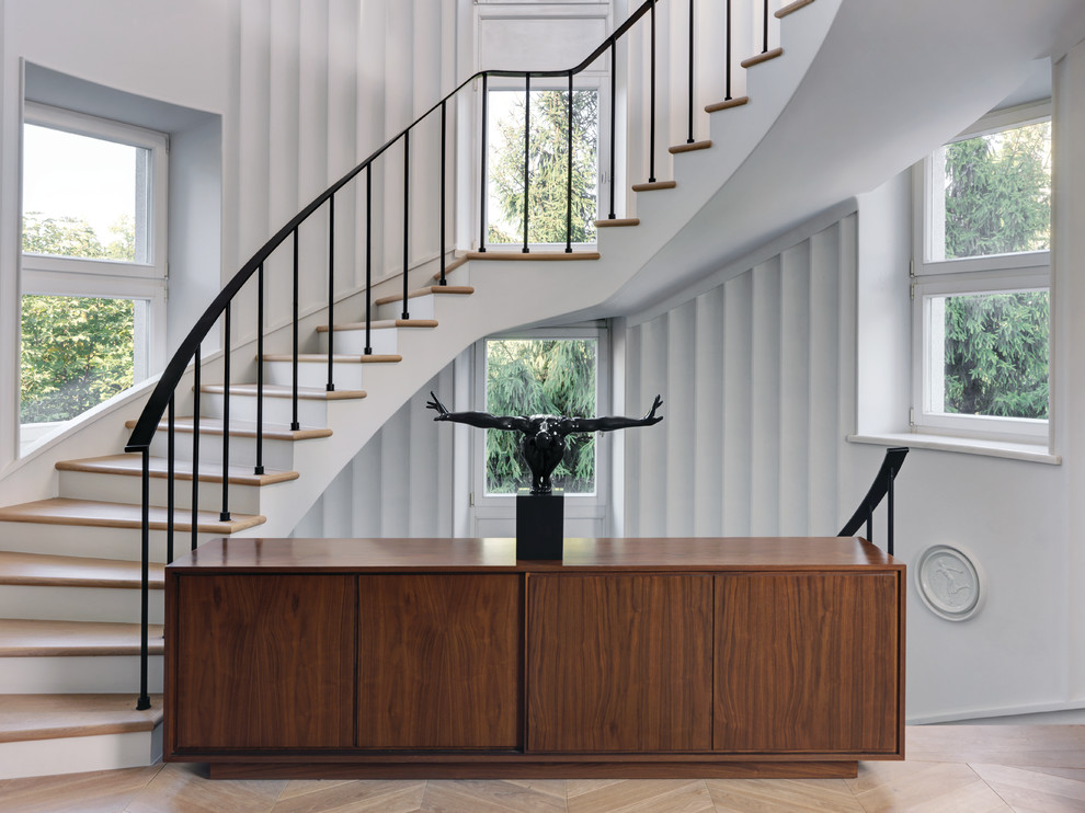 Foto de escalera curva minimalista con escalones de madera, contrahuellas de madera pintada y barandilla de metal